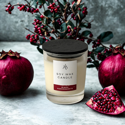 Soy wax candle with a black lid and label, surrounded by pomegranates and berries on a gray surface.