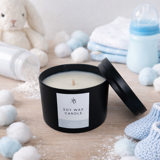 Black soy wax candle with a label surrounded by baby items on a wooden surface